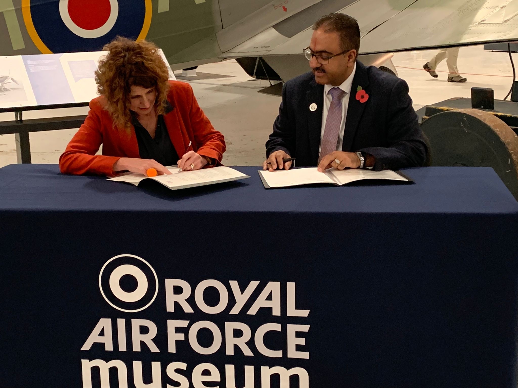 Signing the memorandum of understanding with the RAF Museum Midlands at a table beneath a historic aircraft
