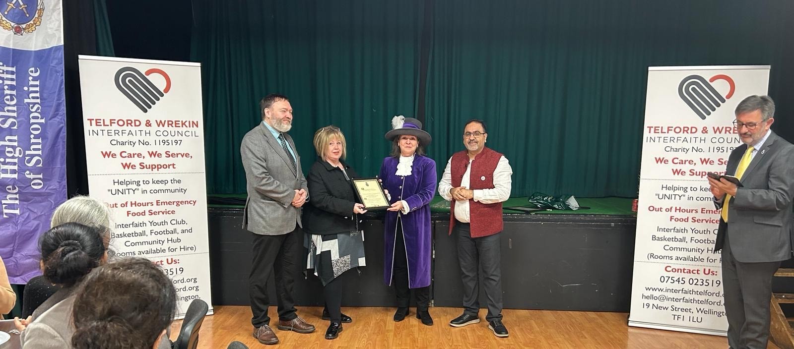 Trustees receiving recognition from the High Sheriff of Shropshire beside Interfaith Council banners