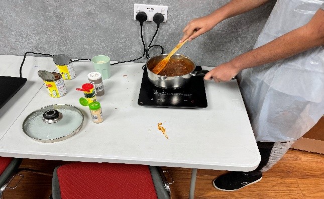 A participant cooking a simple meal on a portable hob during a budgeting and cooking course